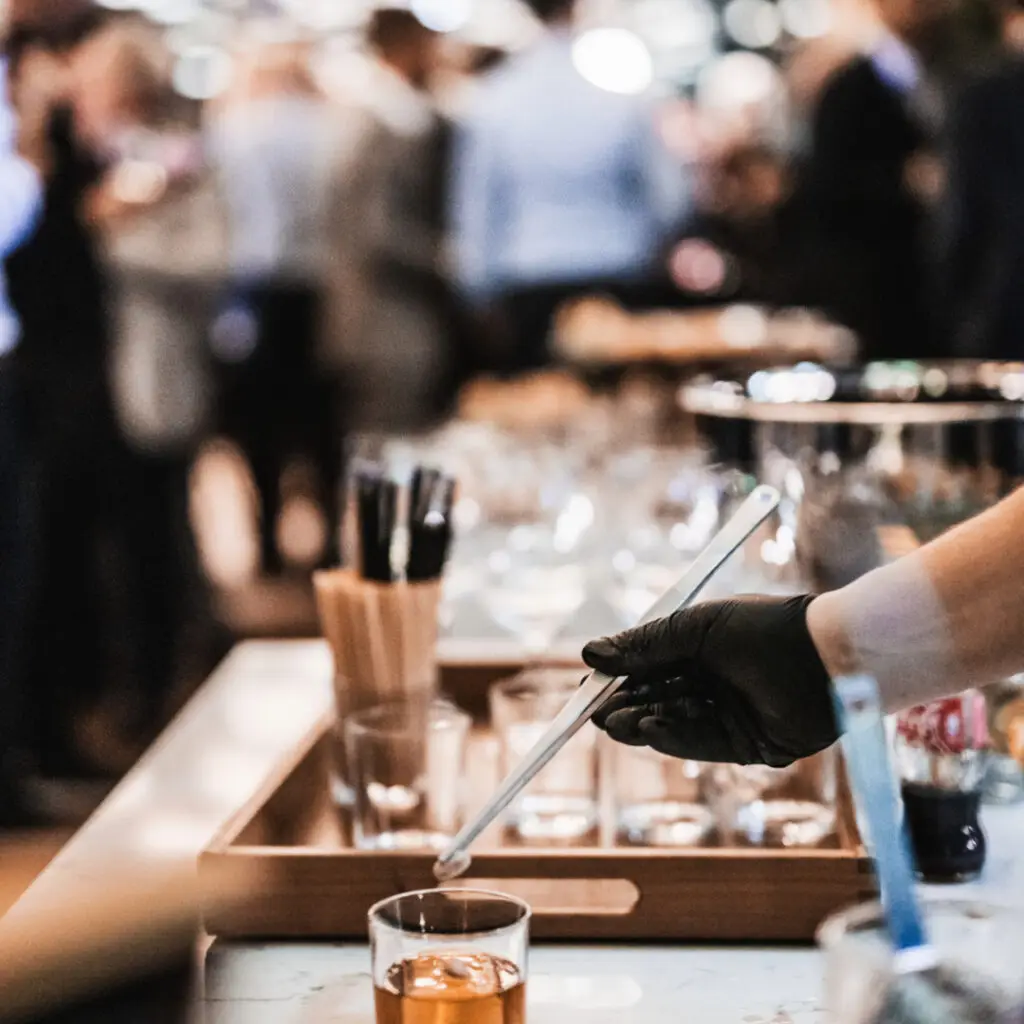 Expert barman is making cocktail at business banquet event in hotel conference center. Blurred businesspeople at banquet event business meeting event in the background